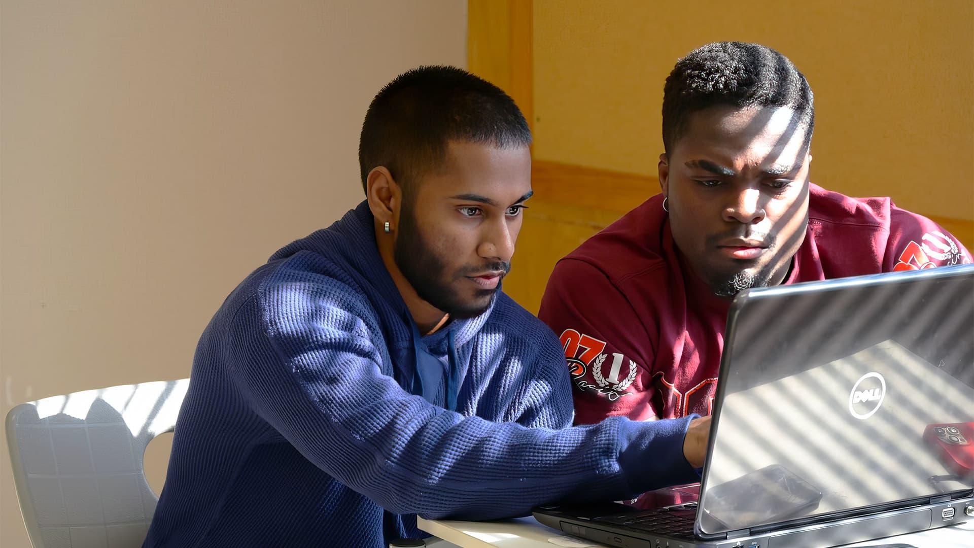 Two male UMFK students sit at a desk together working collaboratively on a laptop