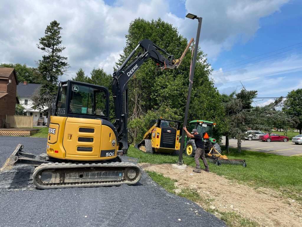 UMFK Facilities Management staff work on installing a light pole at a new parking lot on campus